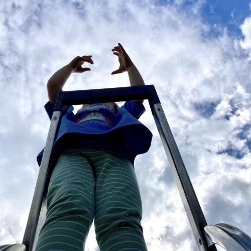 Ein Kind steht auf einem Gerüst und streckt die Arme in den Himmel