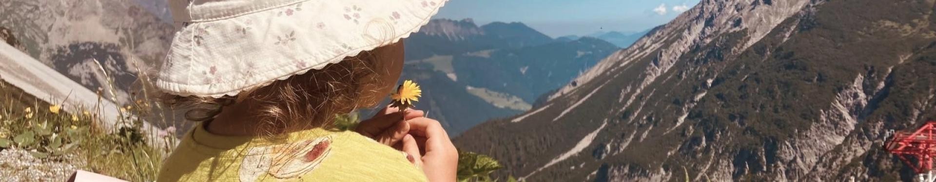 Kind sitzt auf der Wiese und schaut in die Berge